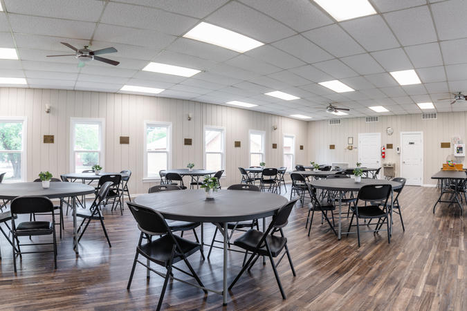 Photo of main room in community center, containing round tables and chairs