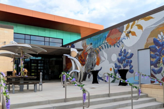 Steps leading to the patio outside the event center. Rails and covered picnic tables are decorated with flower vines. There are cocktail tables near the mosaics and sculpture.