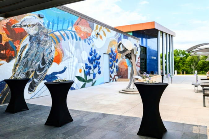 Cocktail tables on the event center patio with a mosaic, sculpture, and main entrance of event center in the background