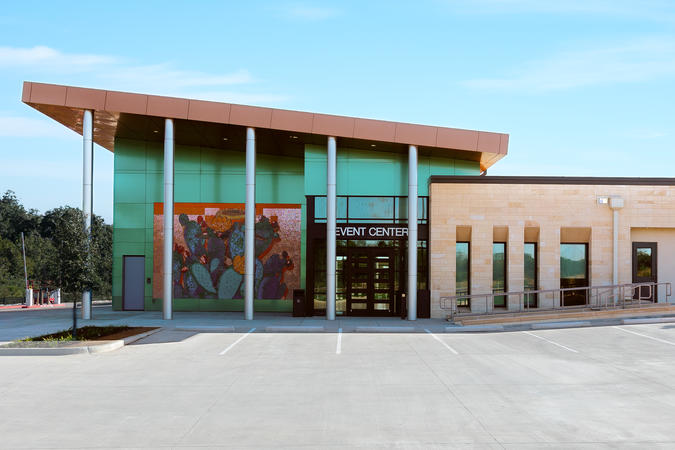 Exterior entrance of the Event Center showing a mural, pillars, and a metallic green and orange facade.
